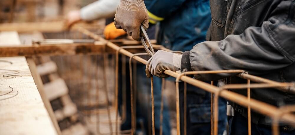 Operários da construção trabalhando na montagem de um quadro de aço em um local de obras.