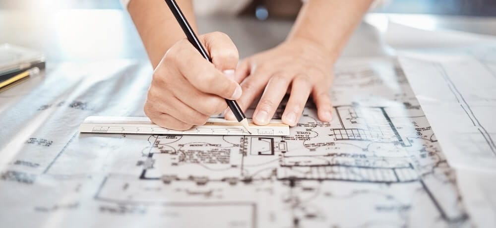 Pessoa desenhando um projeto com um lápis sobre uma mesa, concentrada em detalhes do desenho.