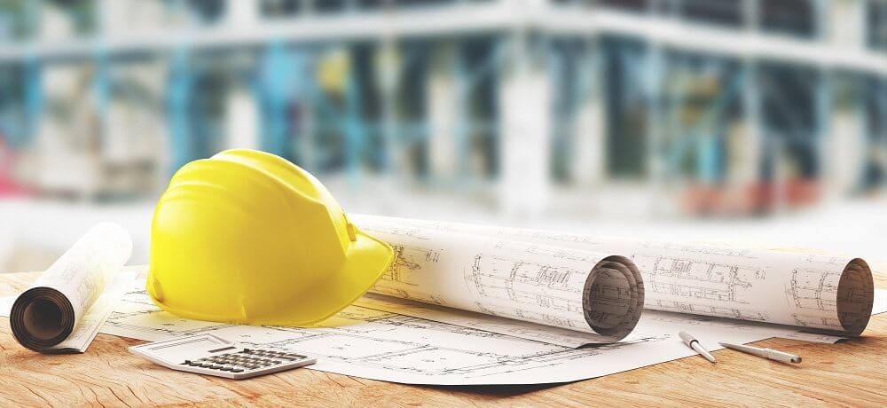 Mesa com planos de construção e um capacete de segurança, simbolizando a preparação para um projeto de construção.